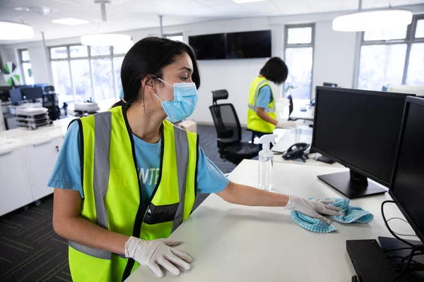 混合种族的女性和同事穿着背心 手套和面罩 用消毒剂在办公室里进行消毒 Coronavirus Covid 19大流行病期间工作场所的卫生 — 图库照片