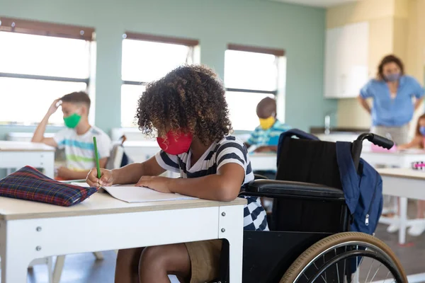 Caucasian female teacher wearing face mask at school, teaching children at school classroom. Education back to school health safety during Covid19 Coronavirus pandemic.