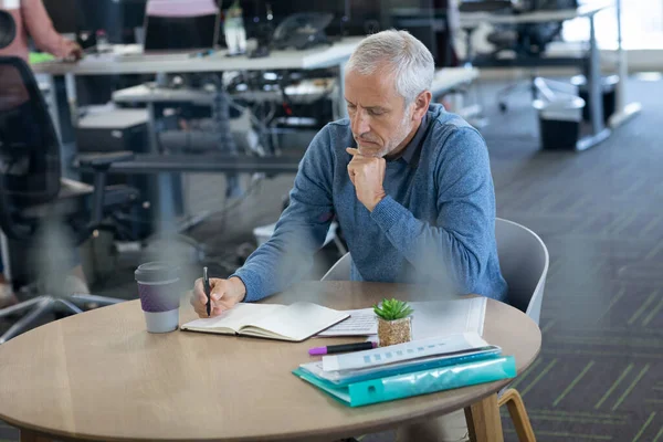 在一个现代化的办公室里 一位资深的高加索商人 坐在桌旁 手里拿着文书工作和咖啡 写着便条 Coronavirus Covid 19大流行病期间工作场所的社会疏离 — 图库照片
