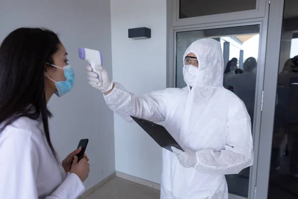 混血女商人 穿着防护服的工人在获准入职前温度测量 Coronavirus Covid 19大流行病期间工作场所的卫生和社会疏离 — 图库照片
