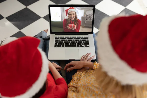 Caucasian woman with her daughter at home at Christmas, using laptop computer, video chatting with another woman. Social distancing during Covid 19 Coronavirus quarantine lockdown.