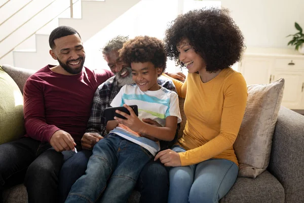 Multi generation African American family at home sitting on sofa in living room, using smartphone, laughing. Family spending quality time at home together in slow motion.