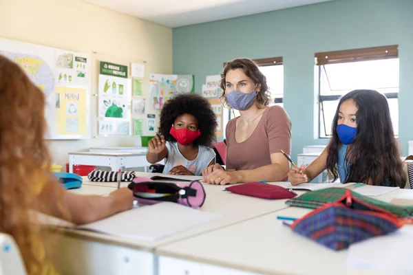 Caucasian female teacher wearing face mask at school, teaching children at school classroom. Education back to school health safety during Covid19 Coronavirus pandemic.