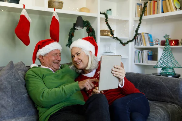 Pareja Mayor Sombreros Santa Sentado Sofá Sonriendo Mirándose Mientras Usa — Foto de Stock