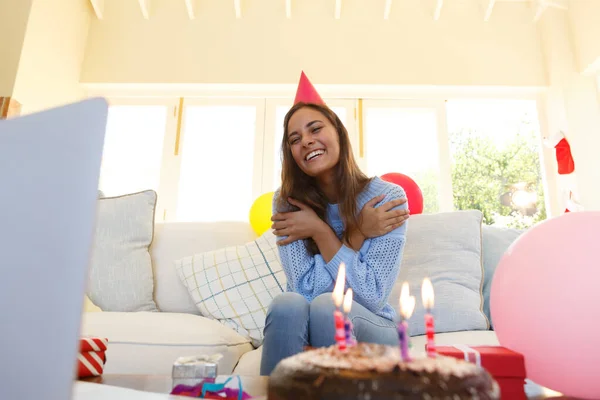 誕生日のビデオ通話を持つ白人女性はパーティー帽子をかぶっている ソファに座ってお誕生日ケーキを前に Covid 19コロナウイルスのパンデミック時の自宅での自己分離 — ストック写真