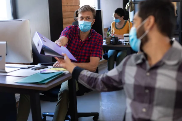 不同的男性同事戴着口罩 在桌子之间传递文件 大肠癌大流行期间工作场所的卫生情况D — 图库照片