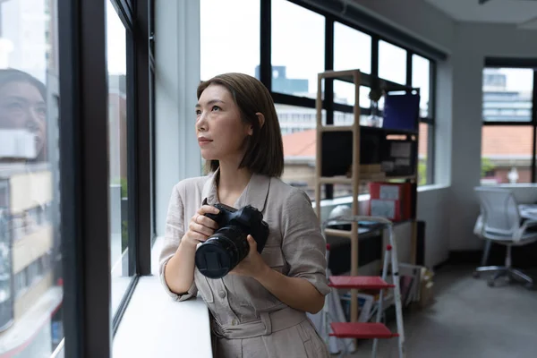 Asian Businesswoman Holding Camera Looking Window Creative Office Social Distancing - Stock-foto