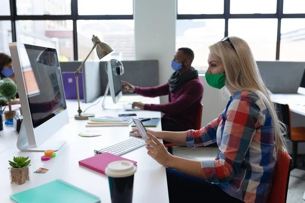 白种人女商人戴着面具坐在办公桌前 在创造性的办公室里使用电脑 大流行病期间工作场所的社会隔离保护卫生 — 图库照片