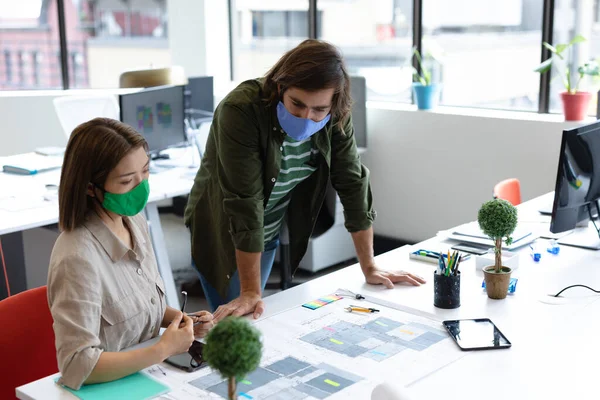 不同的男同事和女同事都戴着面具 看着设计图进行讨论 在流行病蔓延期间 创意办公室的健康保护卫生 — 图库照片