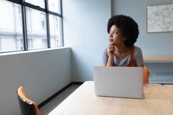 混血女商人在创意办公室工作 坐在桌旁用笔记本电脑的女人 流行病蔓延期间工作场所的社会疏离D — 图库照片