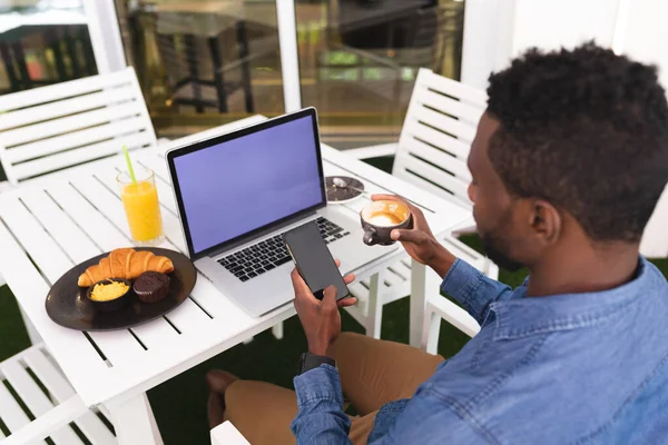 Afrykański Amerykanin Siedzący Kawiarni Przy Użyciu Laptopa Smartfona Pijącego Kawę — Zdjęcie stockowe