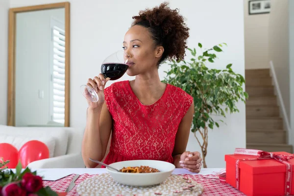 African american woman drinking wine on videocall at home. distant celebration of valentines day online and dating concept