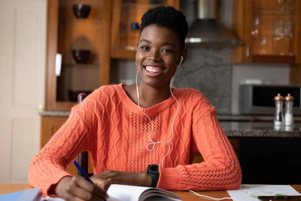 Portrait of african american woman wearing earphones taking notes while working from home. staying at home in self isolation in quarantine lockdown