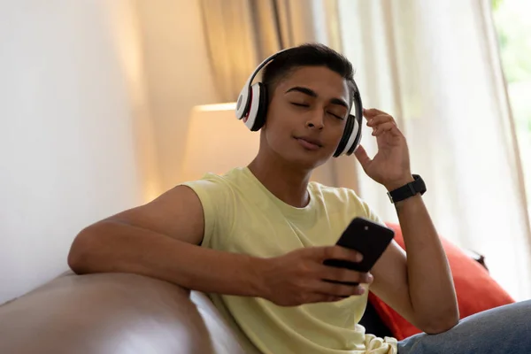 Mieszany Człowiek Rasy Siedzi Kanapie Słuchając Muzyki Pomocą Smartfona Przebywanie — Zdjęcie stockowe