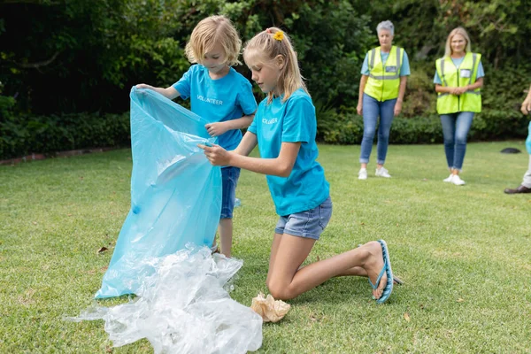 フィールドでプラスチックごみを収集ひざまずいてボランティアグループと白人の男の子と女の子 生態系保全ボランティアが田舎で清掃し — ストック写真