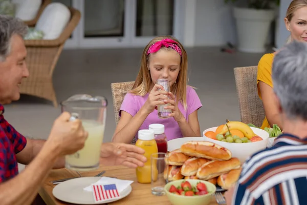 Uśmiechnięta Biała Dziewczyna Pijąca Lemoniadę Rodziną Jedzącą Razem Posiłek Ogrodzie — Zdjęcie stockowe