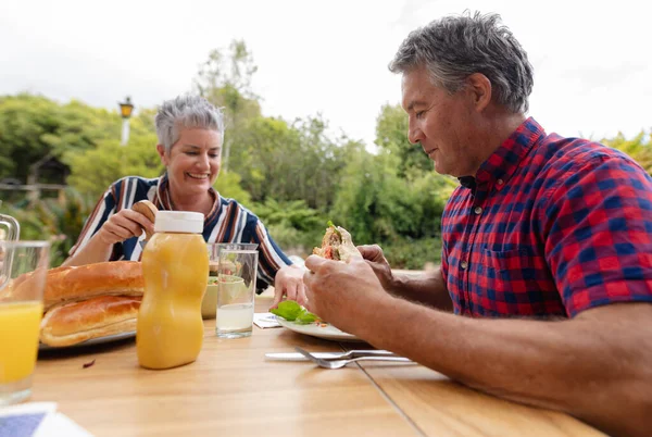 Sonriente Hombre Mayor Caucásico Sosteniendo Hamburguesa Comiendo Comida Con Esposa —  Fotos de Stock