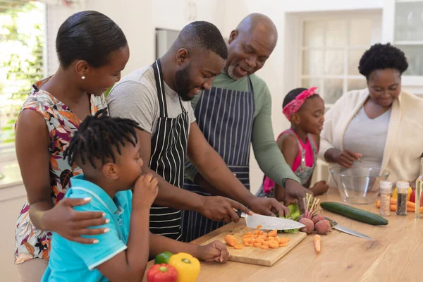 Happy african american parents cooking with son and daughter and grandparents in the kitchen. three generation family spending quality time together.