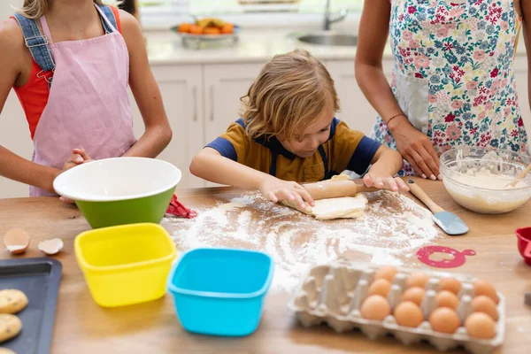 白人男孩在厨房滚动面团与姐姐和母亲一起穿着围裙烘焙饼干 隔离检疫期间单独呆在家里 — 图库照片