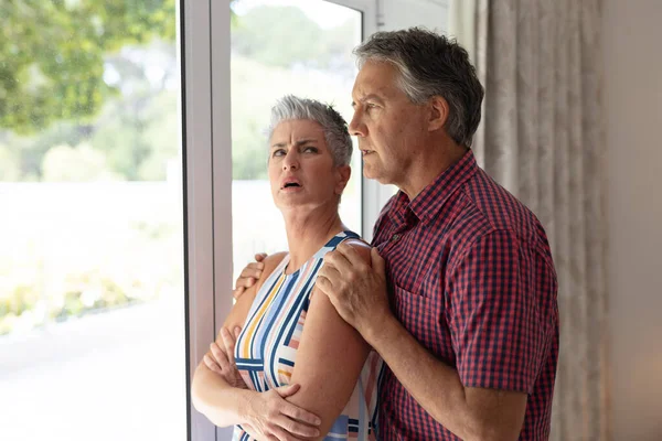 Preocupada Pareja Ancianos Caucásicos Pie Mirando Por Ventana Abrazando Permanecer — Foto de Stock