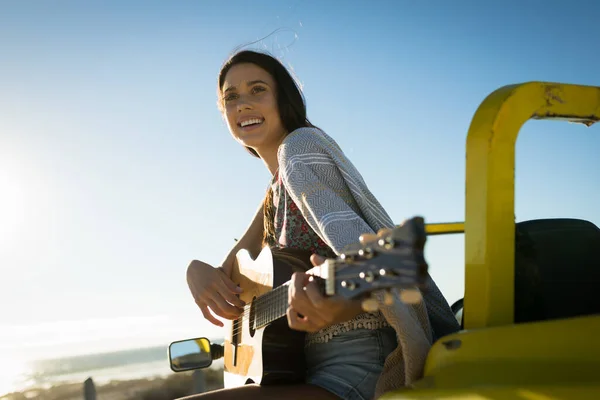 快乐的高加索女人坐在海边的婴儿车上弹吉他 暑假期间的海滩休息 — 图库照片