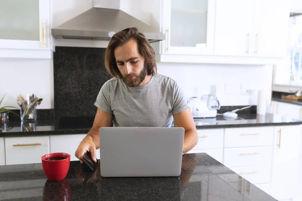 Hombre Caucásico Sentado Cocina Usando Ordenador Portátil Teléfono Inteligente Permanecer — Foto de Stock