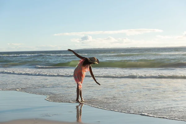 手を広げながら海岸沿いを歩く藁帽子を被った混合レースの女性 海による休暇の屋外レジャータイム — ストック写真