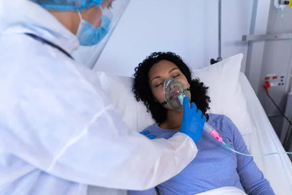 酸素呼吸器を備えた病院のベッドで女性患者をチェックするパイプスーツの白人医師 コロナウイルスにおける医療 医療サービス Covid 19パンデミック — ストック写真
