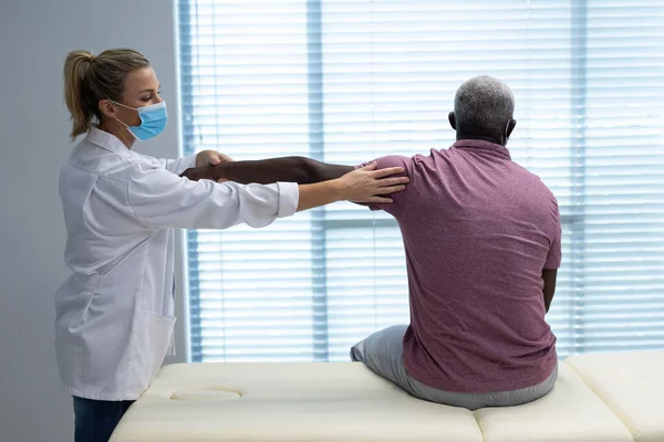 白人女性の理学療法士は アフリカ系アメリカ人男性患者のマスクストレッチ腕を身に着けている コロナウイルスにおける医療 医療サービス Covid 19パンデミック — ストック写真
