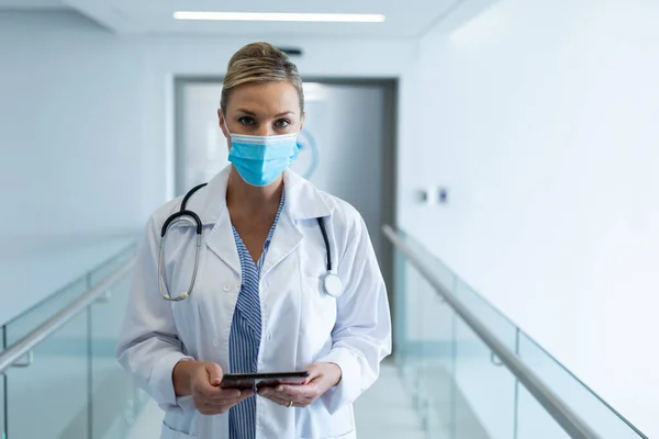病院の廊下でタブレットを保持マスクを身に着けている白人女性医師の肖像画 コロナウイルスにおける医療 医療サービス Covid 19パンデミック — ストック写真