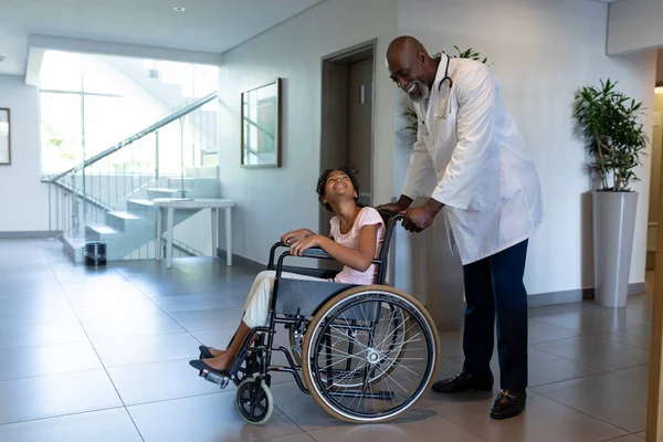 Médico Americano Africano Sorridente Empurrando Menina Raça Mista Cadeira Rodas — Fotografia de Stock