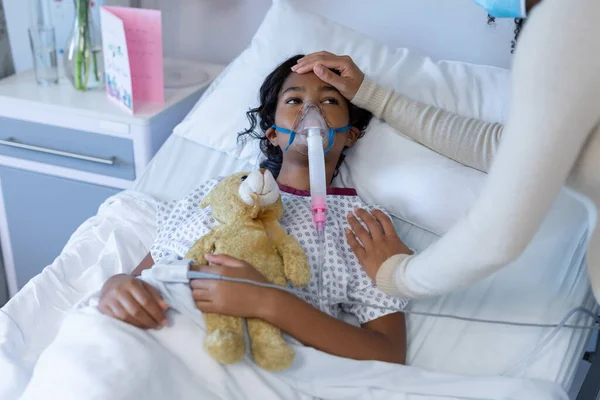 病院の酸素呼吸器に病気の娘の頭に触れる顔マスクの混合レースの母親 コロナウイルスの19大流行時の医療 医療サービス — ストック写真