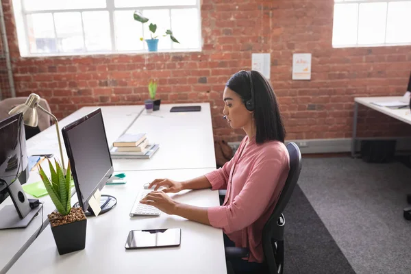 ヘッドフォンを使用してコンピュータの前に座っているビデオ通話を持つ混合レースビジネス女性 独立した創造的なデザインビジネス — ストック写真