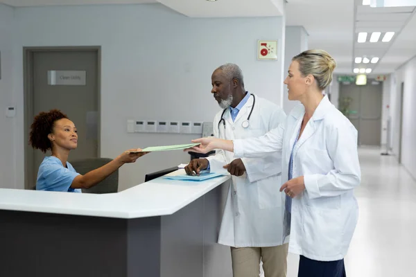 African American Receptionist Passing Document Caucasian Female Doctor Hospital Reception — Stock Photo, Image