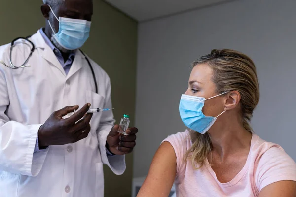 顔面マスクを着用したアフリカ系アメリカ人男性医師は 白人患者のために咳止めワクチンを準備している コロナウイルスCovid 19の間の医学 健康と医療サービス — ストック写真