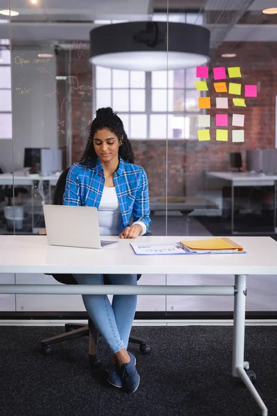 バックグラウンドで壁に粘着性のあるメモをノートパソコンの前に座っている混合レースビジネス女性 独立した創造的なデザインビジネス — ストック写真