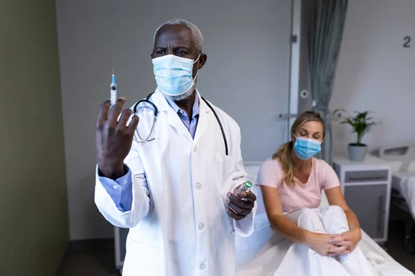顔面マスクを着用したアフリカ系アメリカ人男性医師は 白人患者のために咳止めワクチンを準備している コロナウイルスにおける医療 医療サービス Covid 19パンデミック — ストック写真