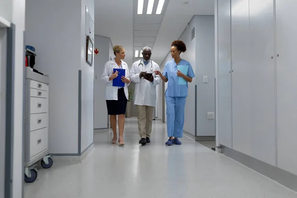 三位不同的男医生和女医生在医院走廊里走来走去 看数字平板电脑 保健和保健服务 — 图库照片