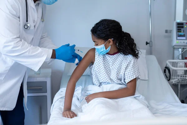 男医生戴着口罩 坐在病床上 给生病的混血女孩注射鱼子酱疫苗 Coronavirus Covid大流行病期间的医疗 保健和保健服务 — 图库照片
