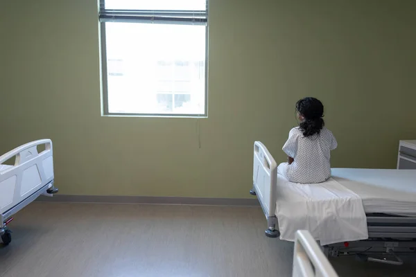 Visão Traseira Menina Mista Doente Sentado Cama Hospital Olhando Para — Fotografia de Stock