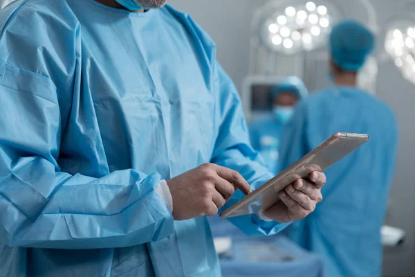 Ameliyathanede Tablet Kullanarak Koruyucu Giysiler Giyen Beyaz Erkek Cerrahın Orta — Stok fotoğraf