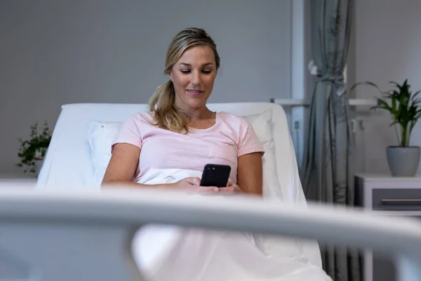 白种人女性病人躺在病床上 用智能手机和微笑 保健和保健服务 — 图库照片
