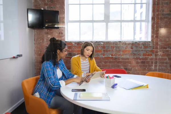 オフィスのテーブルに座ってタブレットを見て議論する多様な女性の同僚 独立した創造的なデザインビジネス — ストック写真