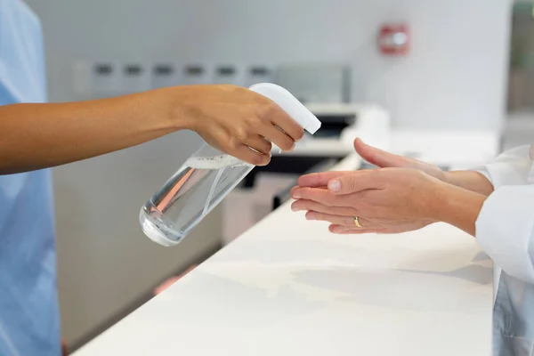 Middel Van Vrouwelijke Receptioniste Desinfecteren Handen Van Een Vrouwelijke Arts — Stockfoto