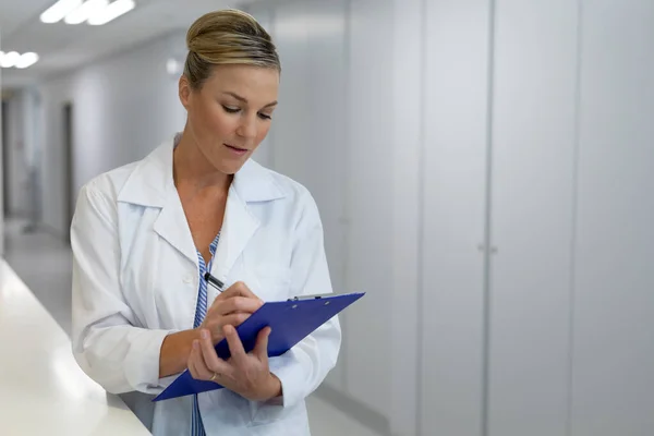 Vit Kvinnlig Läkare Som Står Sjukhuskorridoren Och Fyller Journaldokument Medicin — Stockfoto