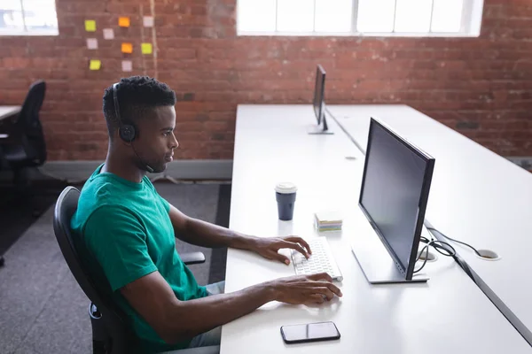 ヘッドフォンを使用してコンピュータの前にオフィスに座っているアフリカ系アメリカ人ビジネスマン そうだ 独立した創造的なデザインビジネス — ストック写真