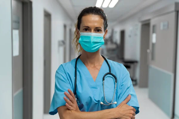 身穿面罩的混血女医生站在医院走廊上的画像 Coronavirus Covid大流行病期间的医疗 保健和保健服务 — 图库照片