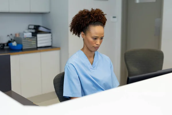 アフリカ系アメリカ人女性の受付員は 病院の受付でコンピュータを使って机に座っている 医療サービス — ストック写真