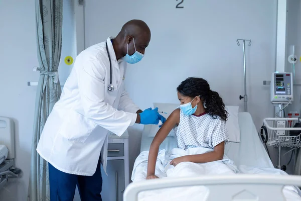 非洲裔美国男性医生 戴着口罩 在医院病床上给生病的女孩注射牛皮癣疫苗 Coronavirus Covid大流行病期间的医疗 保健和保健服务 — 图库照片