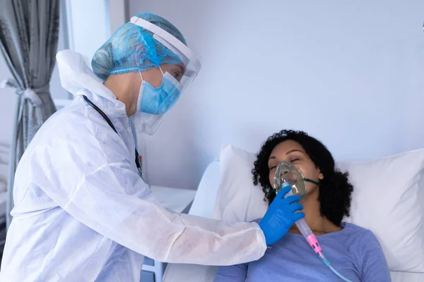 人工呼吸器を装着したアフリカ系アメリカ人女性患者を確認するパイプスーツを着た白人女性医師 コロナウイルスにおける医療 医療サービス Covid 19パンデミック — ストック写真